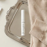 Skincare product on a silver tray with a beige sweater and jewelry on a white surface