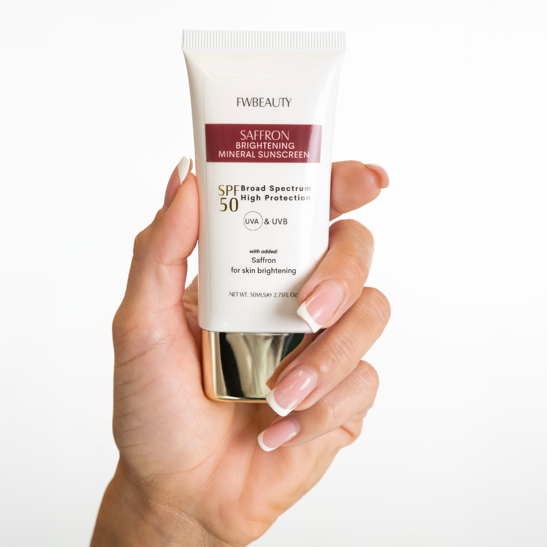 Hand holding a tube of FwBeauty Saffron Brightening Mineral Sunscreen on a white background