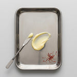 Metal tray with a spread of yellow cream, a knife, and saffron on a light gray background