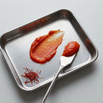 Metal tray with tomato paste, saffron, and a spoon on a light gray background