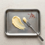 Metal tray with spreadable food, a knife, and red chili peppers on a light background