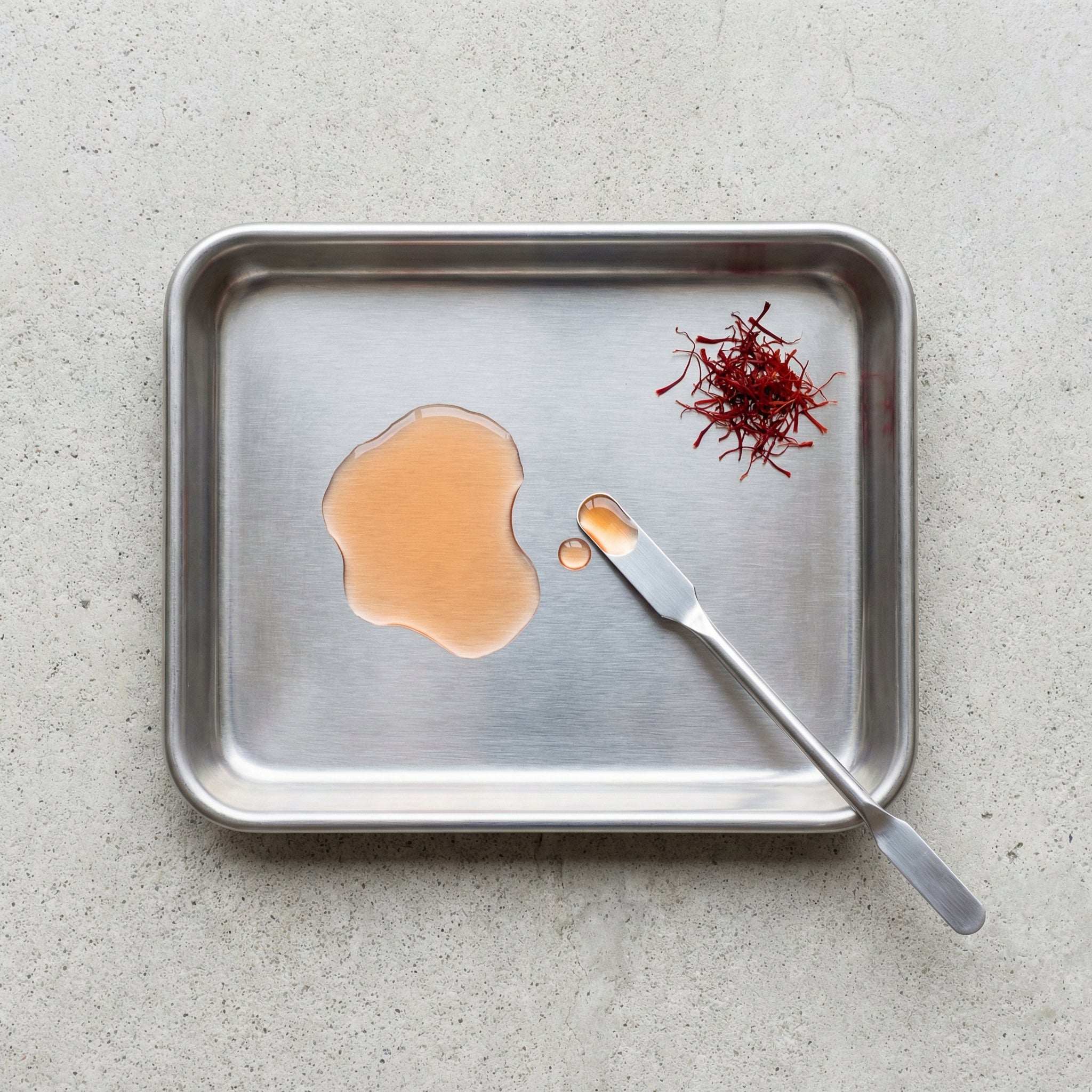 Metal tray with saffron threads and a dollop of liquid on a light gray background