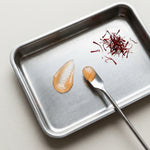 Metal tray with saffron threads and two droplets of lip oil on a light background