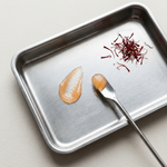 Metal tray with saffron threads and two droplets of liquid on a light background