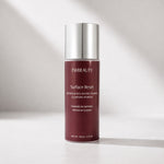 FWBEAUTY Surface Reset Cleansing Powder in a matte burgundy bottle with a reflective silver cap, set against a warm, softly lit gray background.