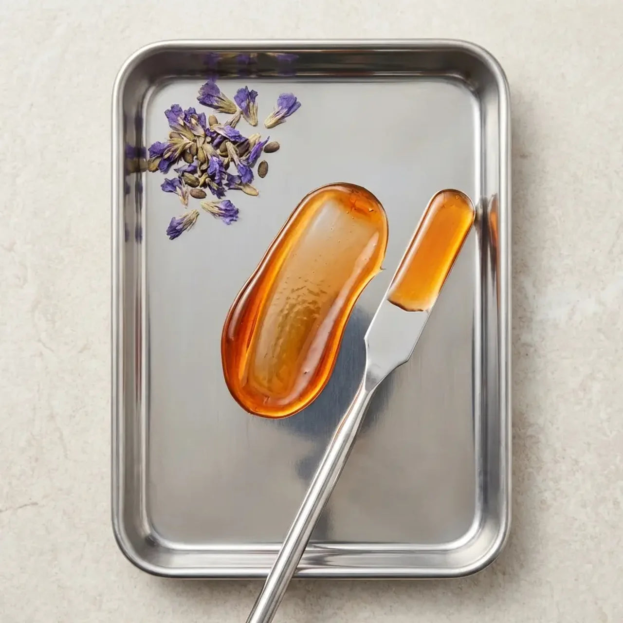 Butter knife with a pat of amber-colored butter on a metal tray with lavender flowers.