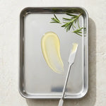 Butter with a knife on a metal tray with rosemary leaves on a light background