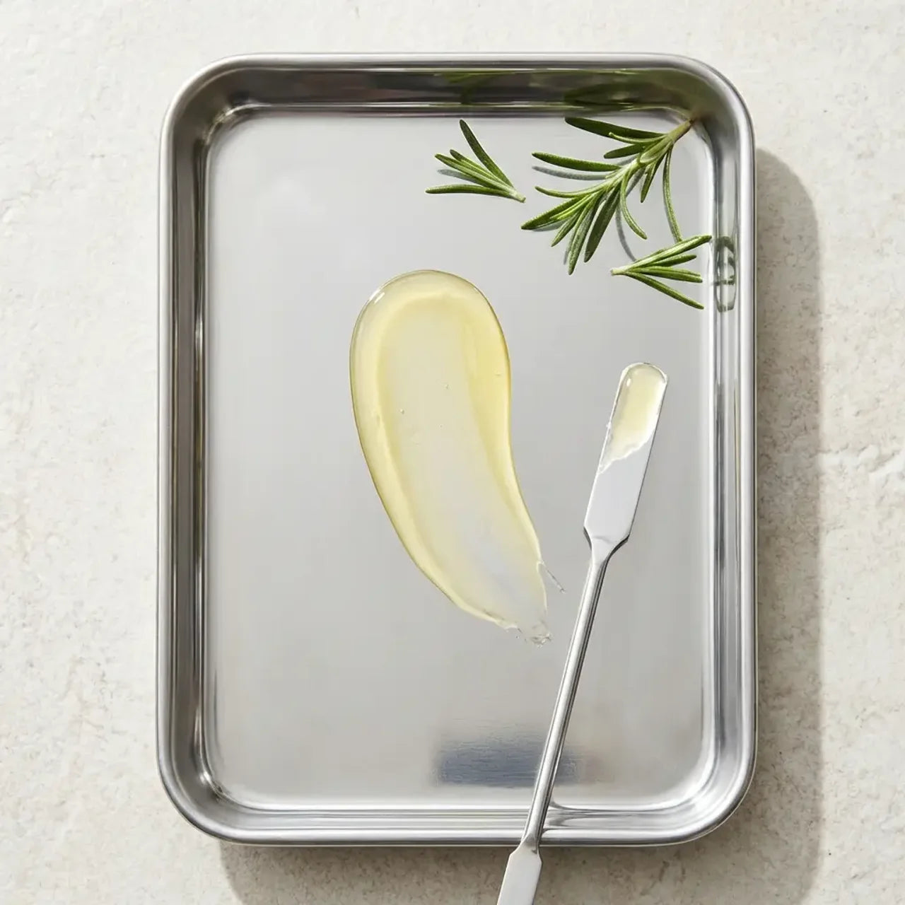 Butter with a knife on a metal tray with rosemary leaves on a light background