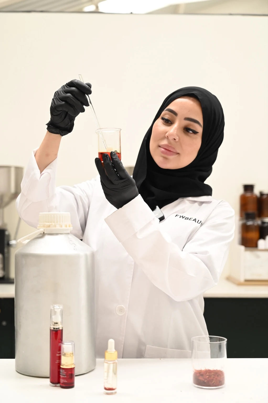 Fatiha Rouf in the FWBEAUTY production lab, examining saffron extract in a beaker, shown in black and white